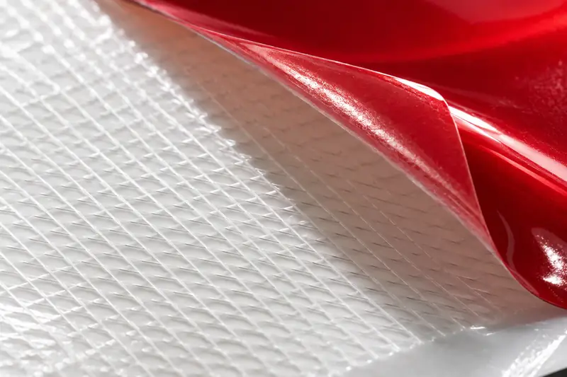 Macro of a vinyl release liner with air-release channels and red film peeled back